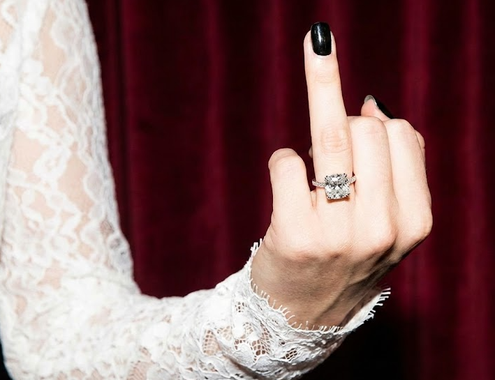 Bride in White Lace Dress Showing Off Diamond Ring & Black Nail Polish in Front of Red Velvet Curtain Wedding Decor