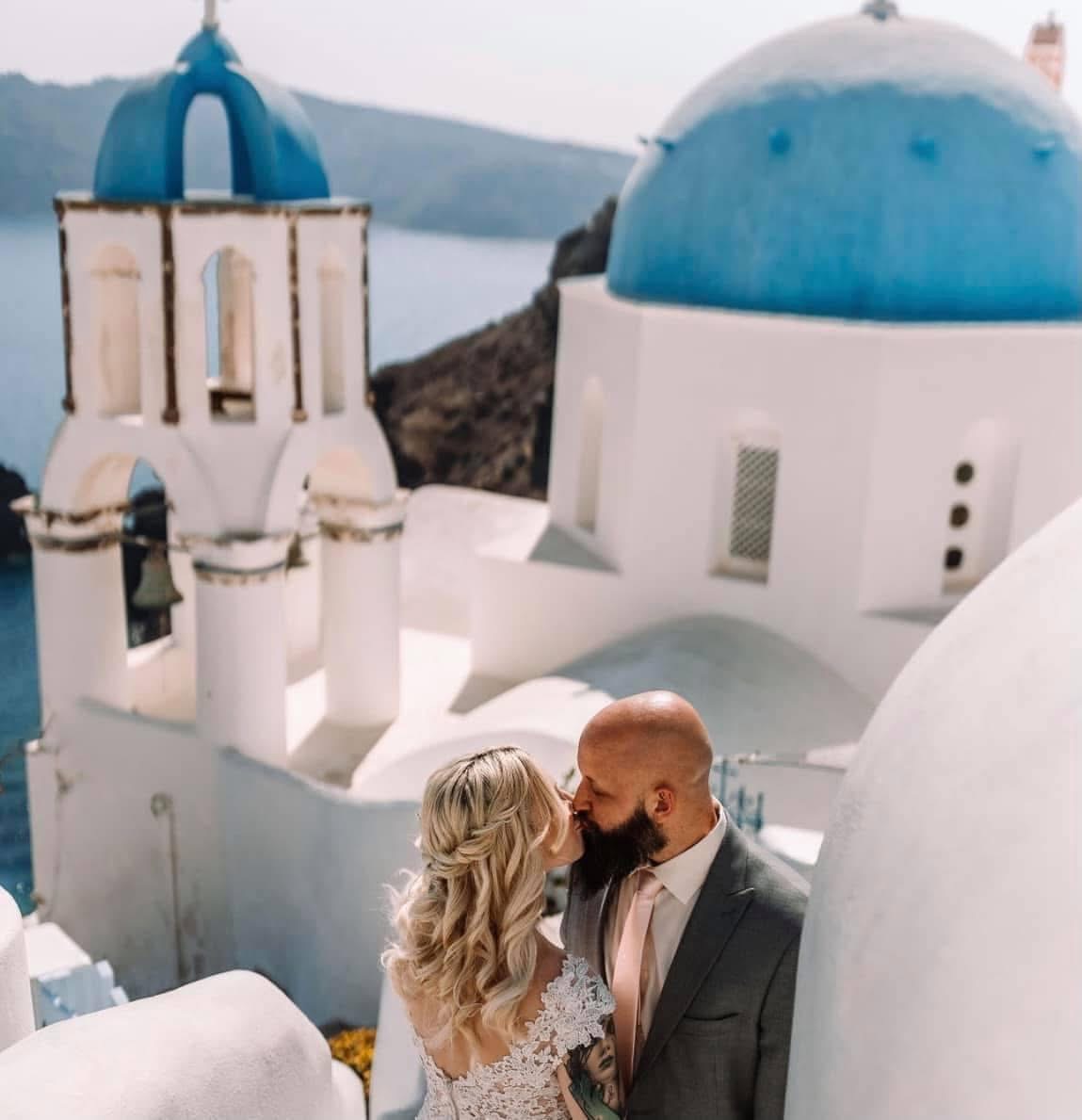Destination Wedding Couple Embracing In Front of Blue Santorini Domes